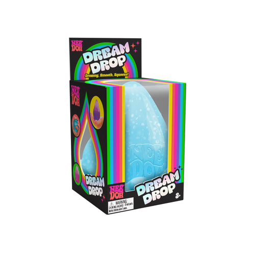 A Dream Drop V2 in its packaging. The packaging is primarily black with rainbow-colored accents and text that reads "Dream Drop" and " ". The toy inside is a blue, drop-shaped, squeezable item. Suitable for ages 3 and up.